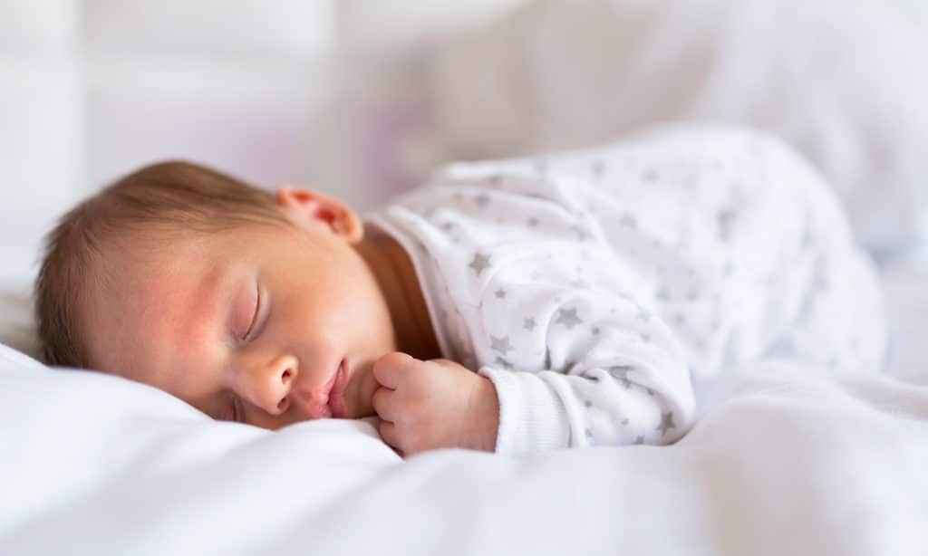 A sleeping newborn baby on a white blanket