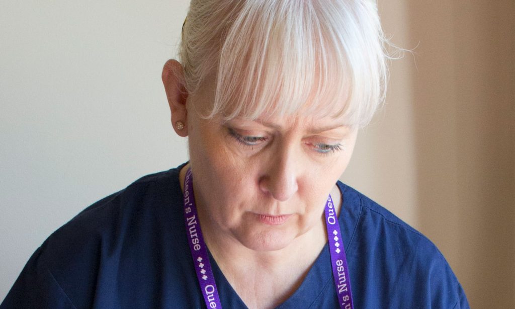 A District Nurse looks downwards with a serious expression