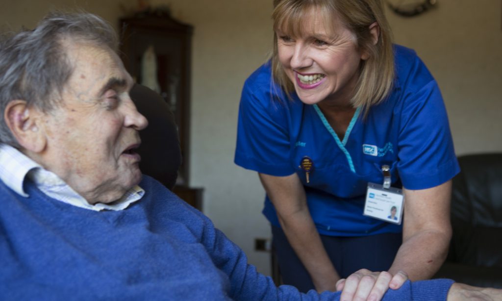 A nurse smiles and chats with an elderly man on a home visit