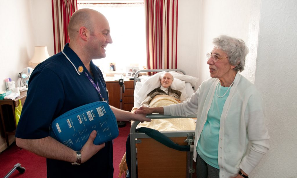 A District Nurse chats with a carer when visiting her husband at home