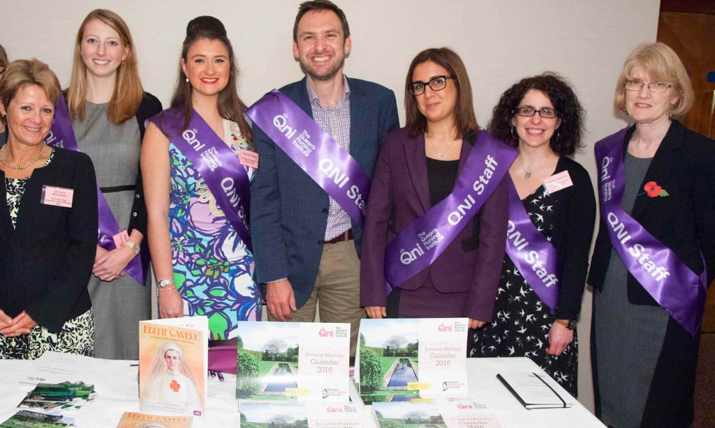 A group of QNI staff at an exhibition stand wearing purple QNI sashes