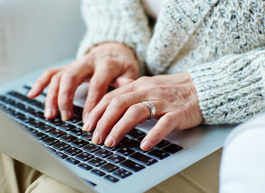 Older hands typing on a laptop keyboard