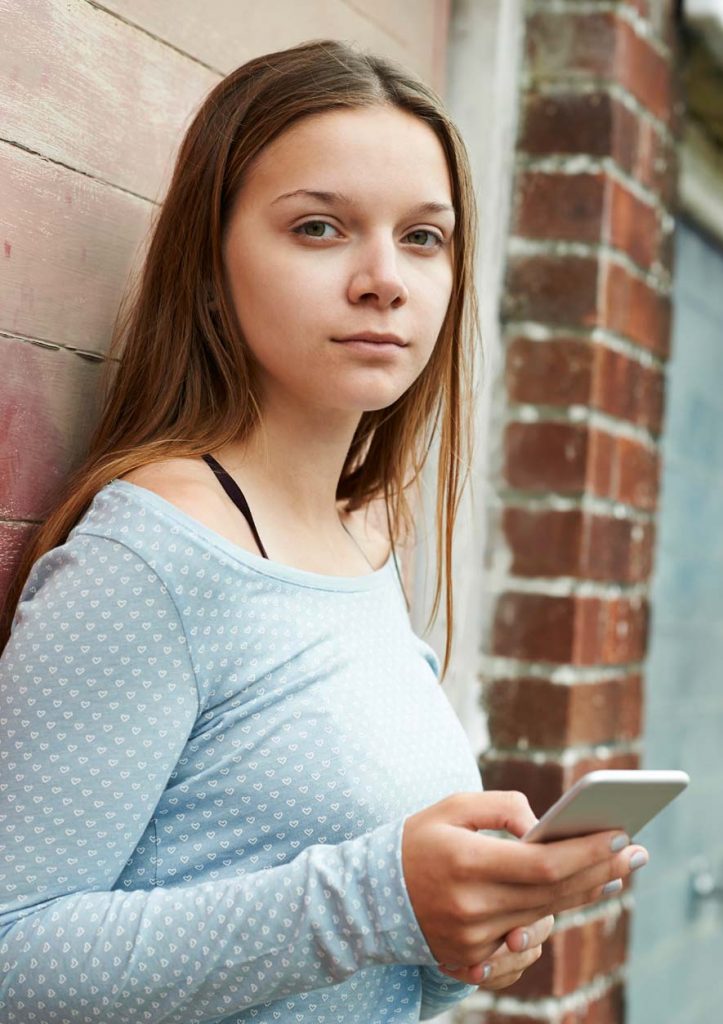 A teenage girl looks to camera with a mobile phone in her hands