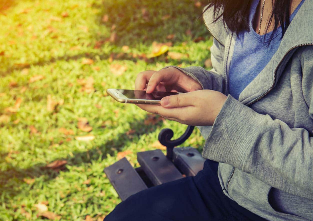 A teenager using a mobile phone sits on a park bench