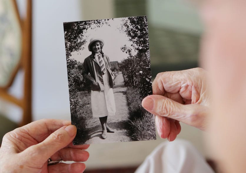 An older person holds a black and white photograph of themselves as a schoolgirl