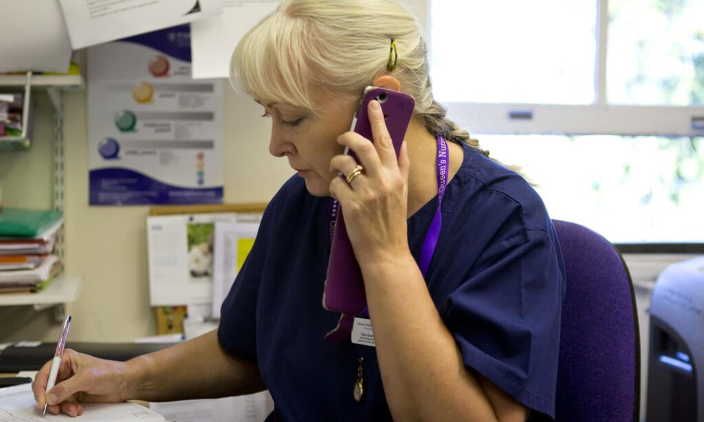 A nurse taking a phone call at her desk making notes